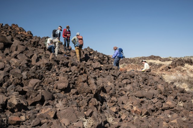 A group of people stand on a incline with lava rocks.