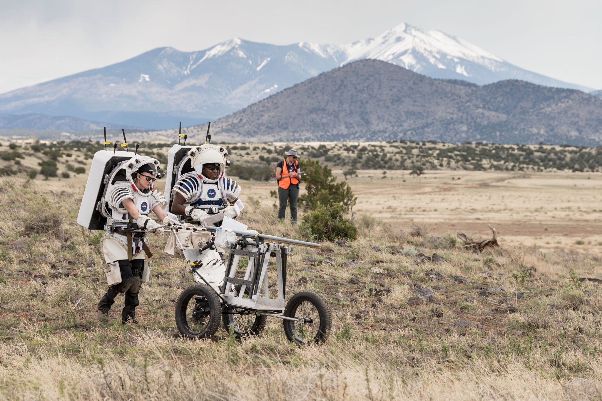 NASA astronauts Kate Rubins and Andre Douglas push a tool cart loaded with lunar tools through the San Francisco Volcanic Field north of Flagstaff, Arizona, as they practice moonwalking operations for Artemis III.