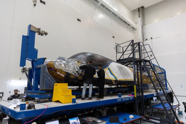 Sierra Space Dream Chaser spacecraft is on a processing platforms with crew members assessing it.