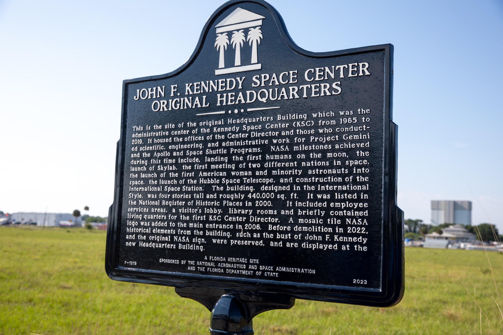 A bronze placard with white words is centered among a backdrop of clouds and grass.