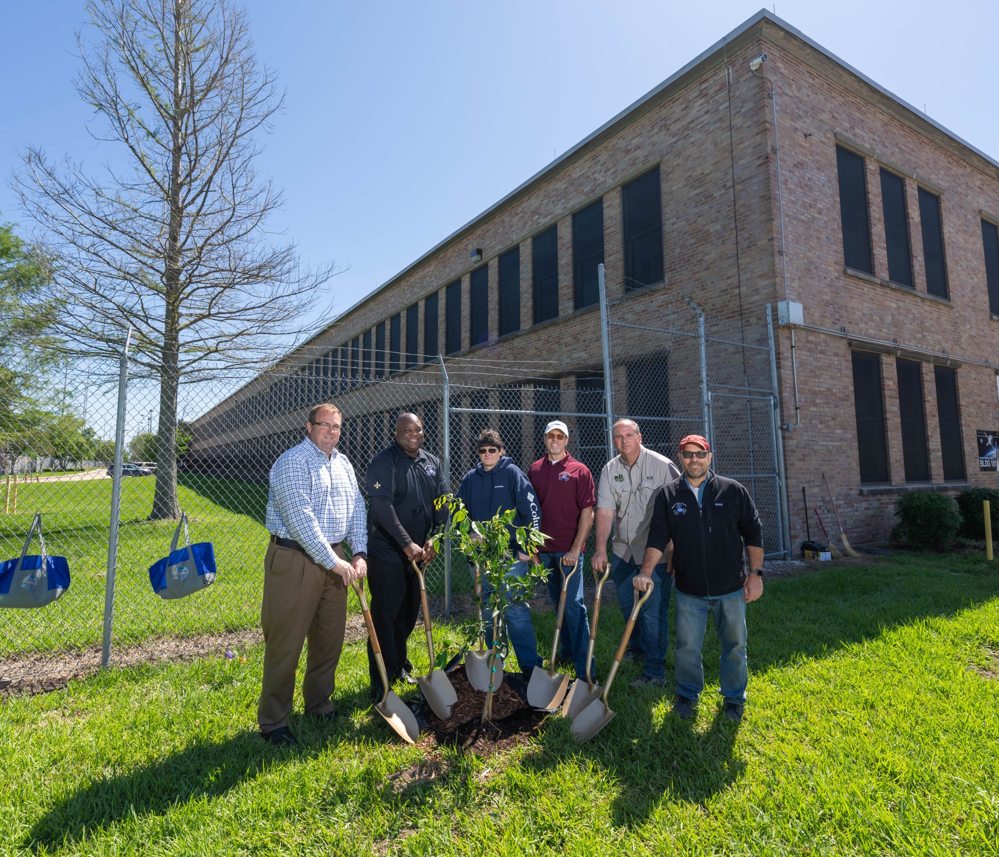 From left, Boeing Michoud Deputy Site Leader Brad Saxton, Michoud Assembly Facility Director Hansel Gill, Textron Supervisor Inventory Control/Shipping MAF/Stone Road Wendy Dedeaux, Lockheed Martin Environmental Health and Safety Engineer Darrell Christian, Michoud Environmental Officer Ben Ferrell, and Syncom Space Services Environmental Manager Eric Stack pack in dirt and mulch around a newly planted satsuma tree at Michoud.
