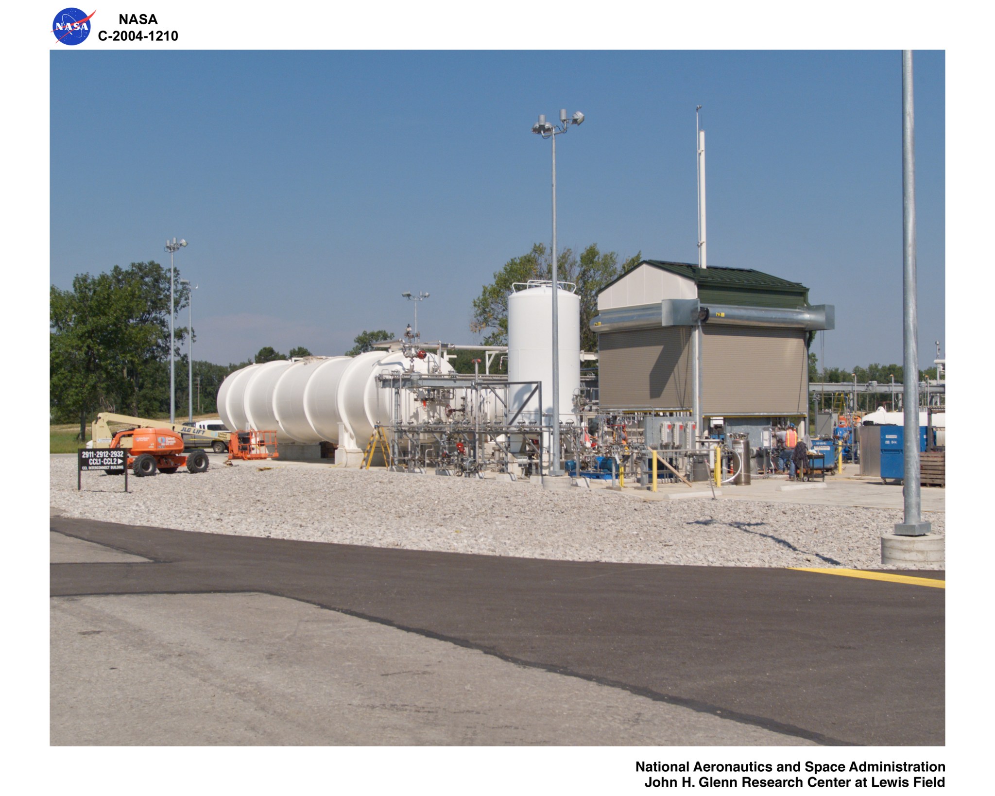 This external view of the facility includes two large white cylinders, one horizonal and one vertical. A small square building next to them, and many components in front for hook up.