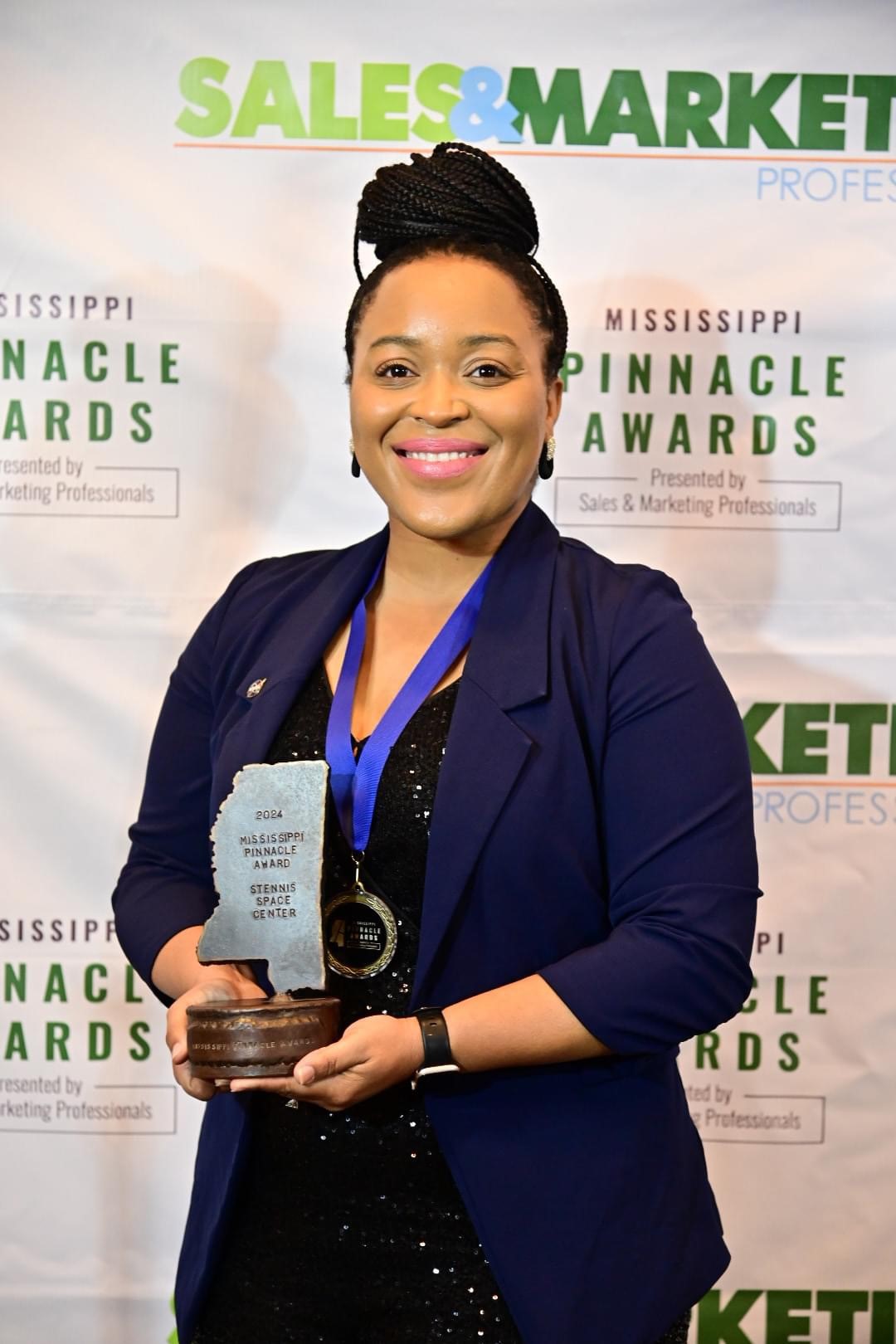 NASA Public Affairs Specialist Samone Wilson, wearing a black jacket, holds a Pinnacle Award while smiling at the camera.