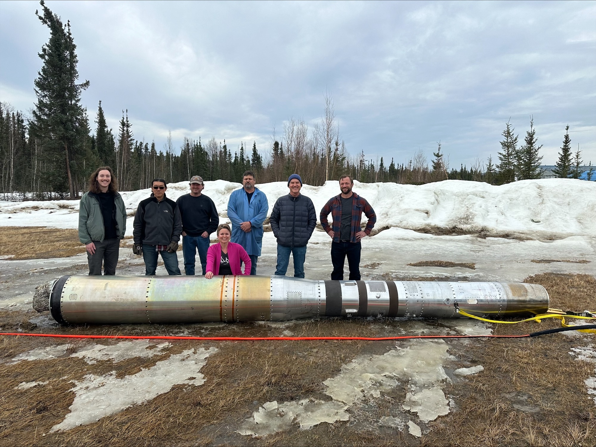 A group of people stand behind a sounding rocket.