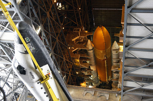 In the Vehicle Assembly Building (VAB) at NASA’s Kennedy Space Center in Florida, workers lift Atlantis to mate it to its External Tank and Solid Rocket Boosters
