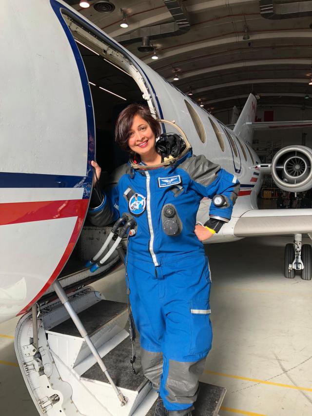 An Indian woman wearing a blue flight suit stands on the steps of a small jet.
