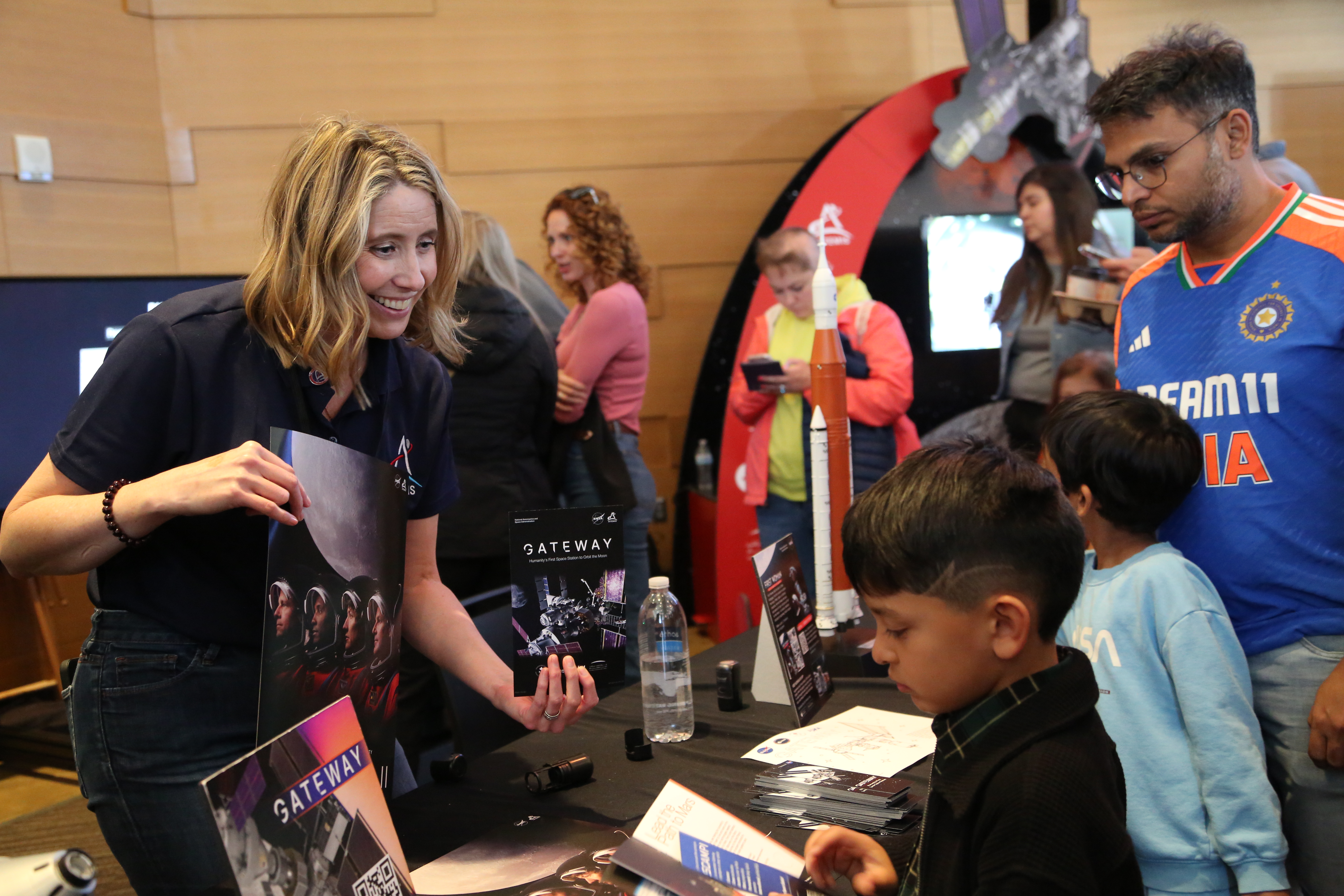 A NASA representative smiles while handing out Gateway Program materials to a young attendee at a NASA booth during the CreateSpace event at the Au...