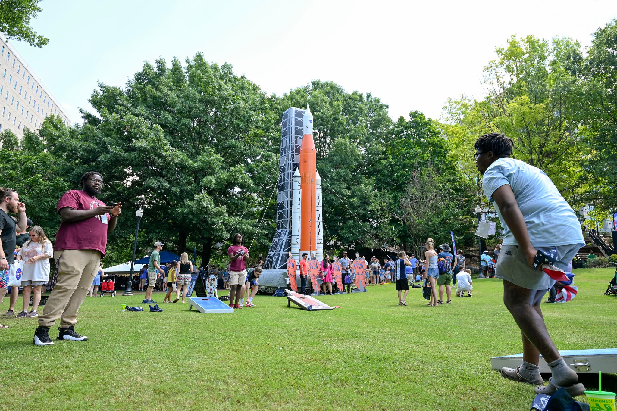 Visitors to NASA in the Park participate in a game of cornhole in front of a display featuring Artemis and NASA’s SLS (Space Launch System).