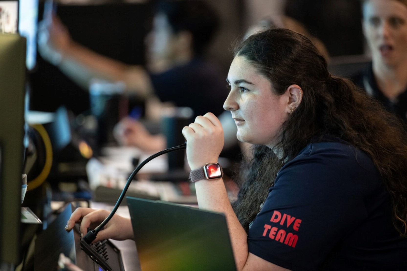 A woman wearing a shirt that says "dice team" speaks into a control room microphone.