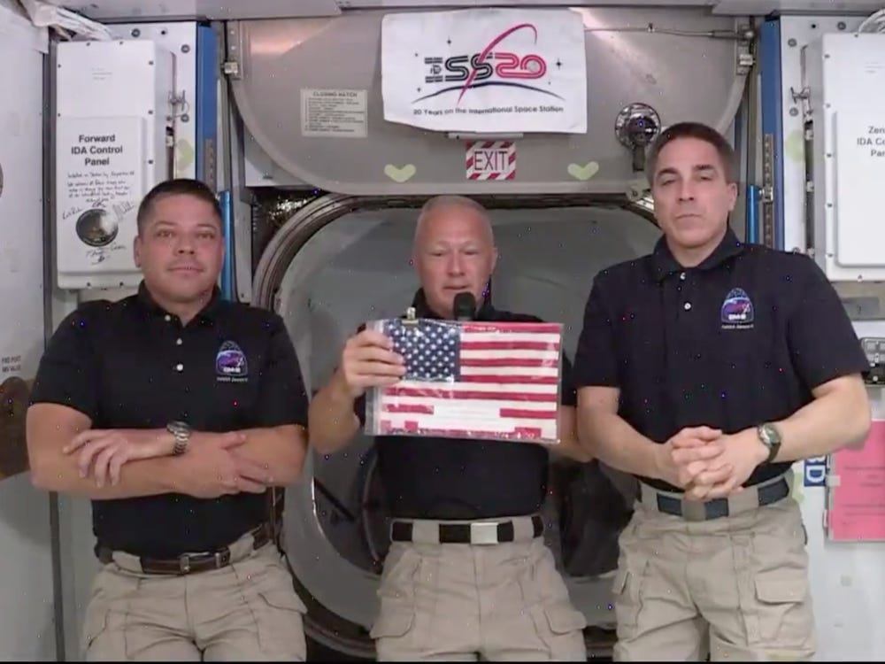 NASA astronauts Robert L. Behnken, left, Douglas G. Hurley (holding the Legacy Flag), and Christopher J. Cassidy during a press conference
