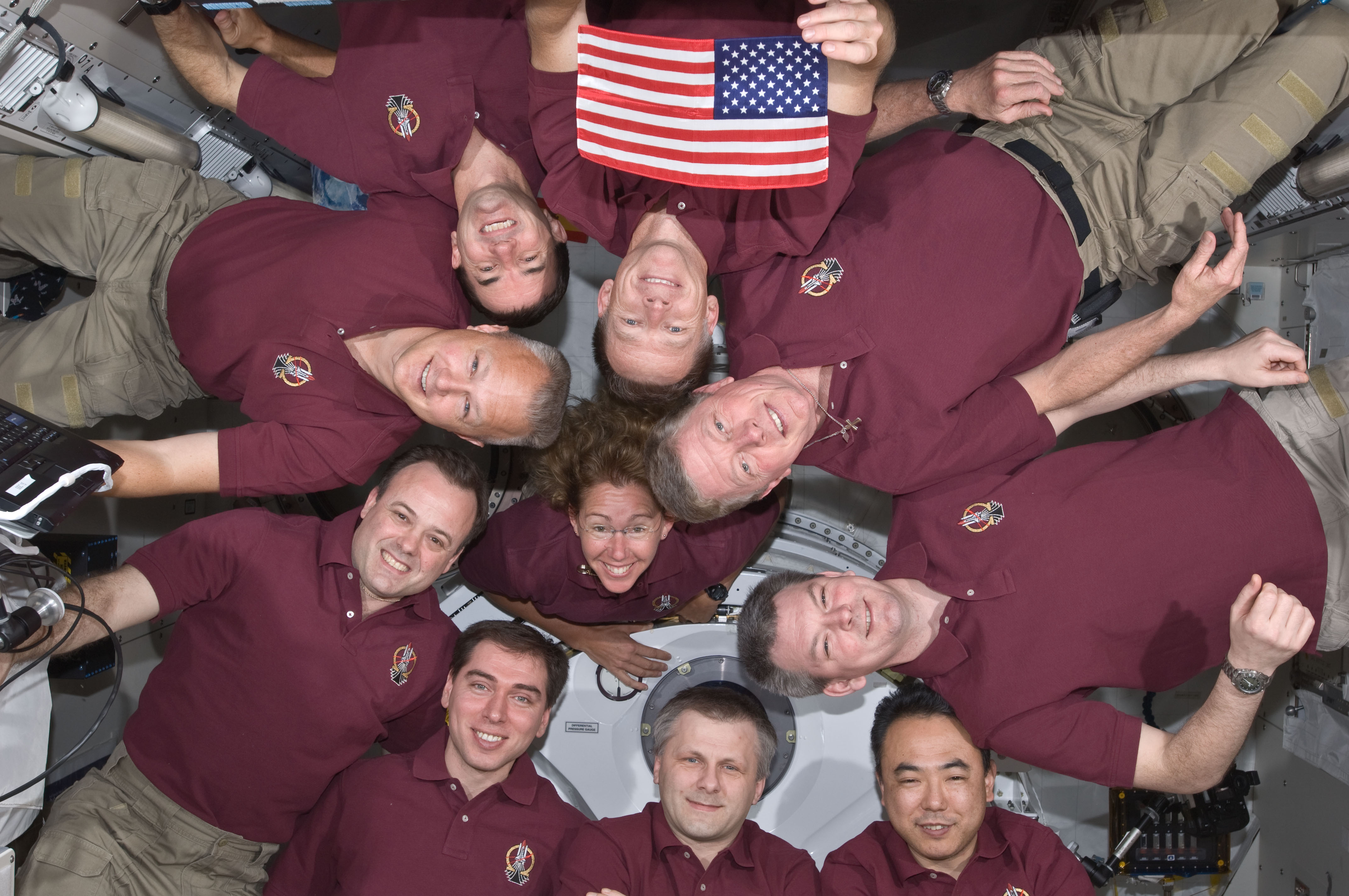 The crews of STS-135 and Expedition 28 pose with the Legacy Flag