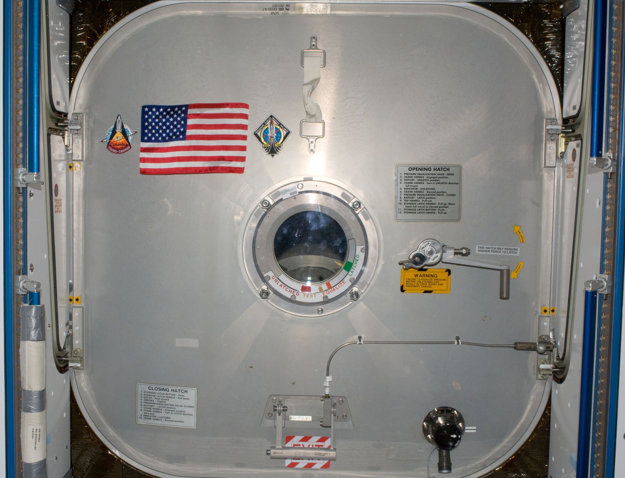 The crews of STS-135 and Expedition 28 place the Legacy Flag on the hatch of the Harmony module
