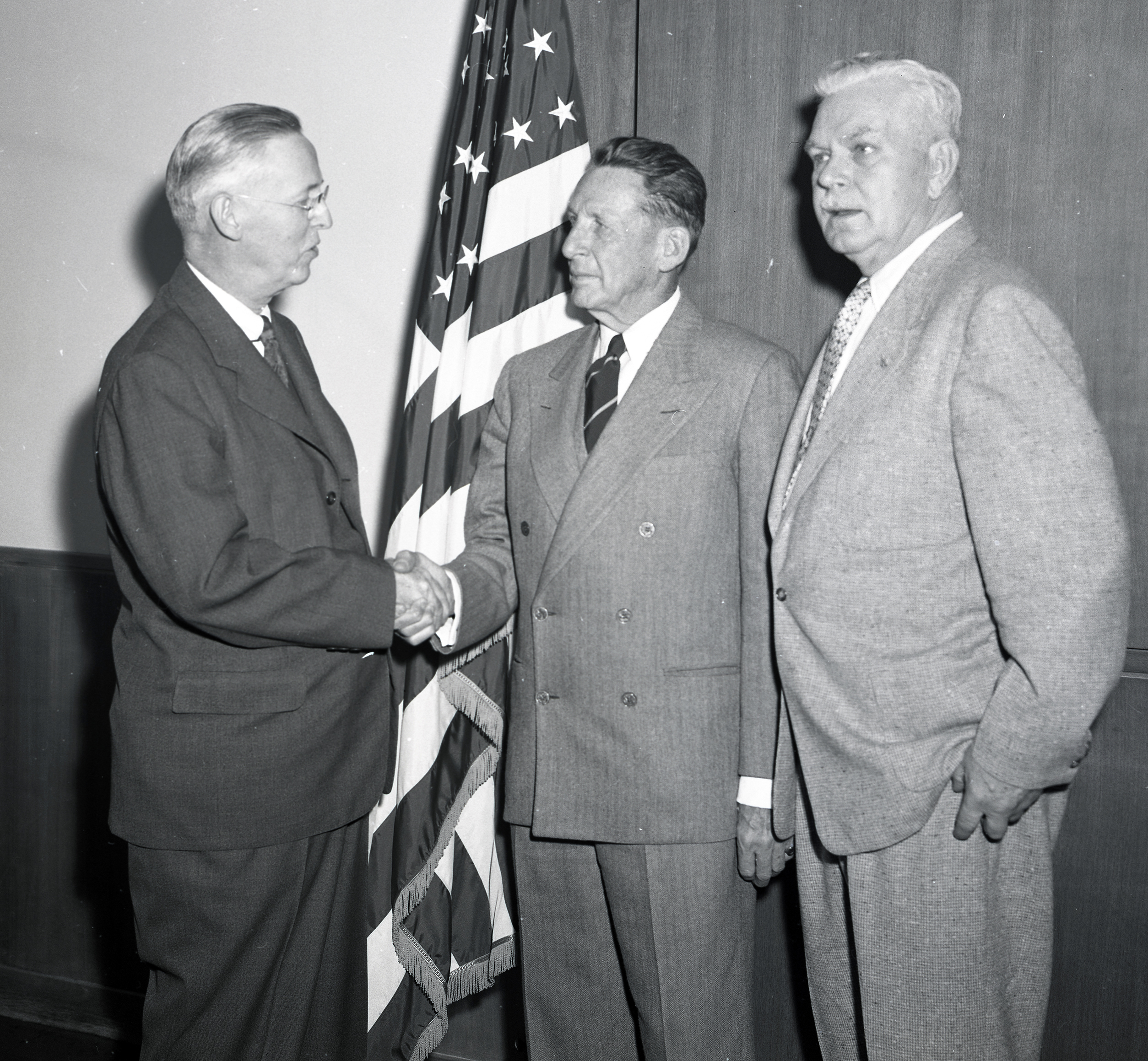 Three men standing by flag.