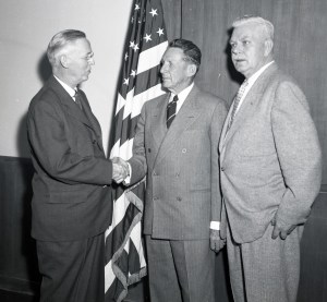 Three men standing by flag.