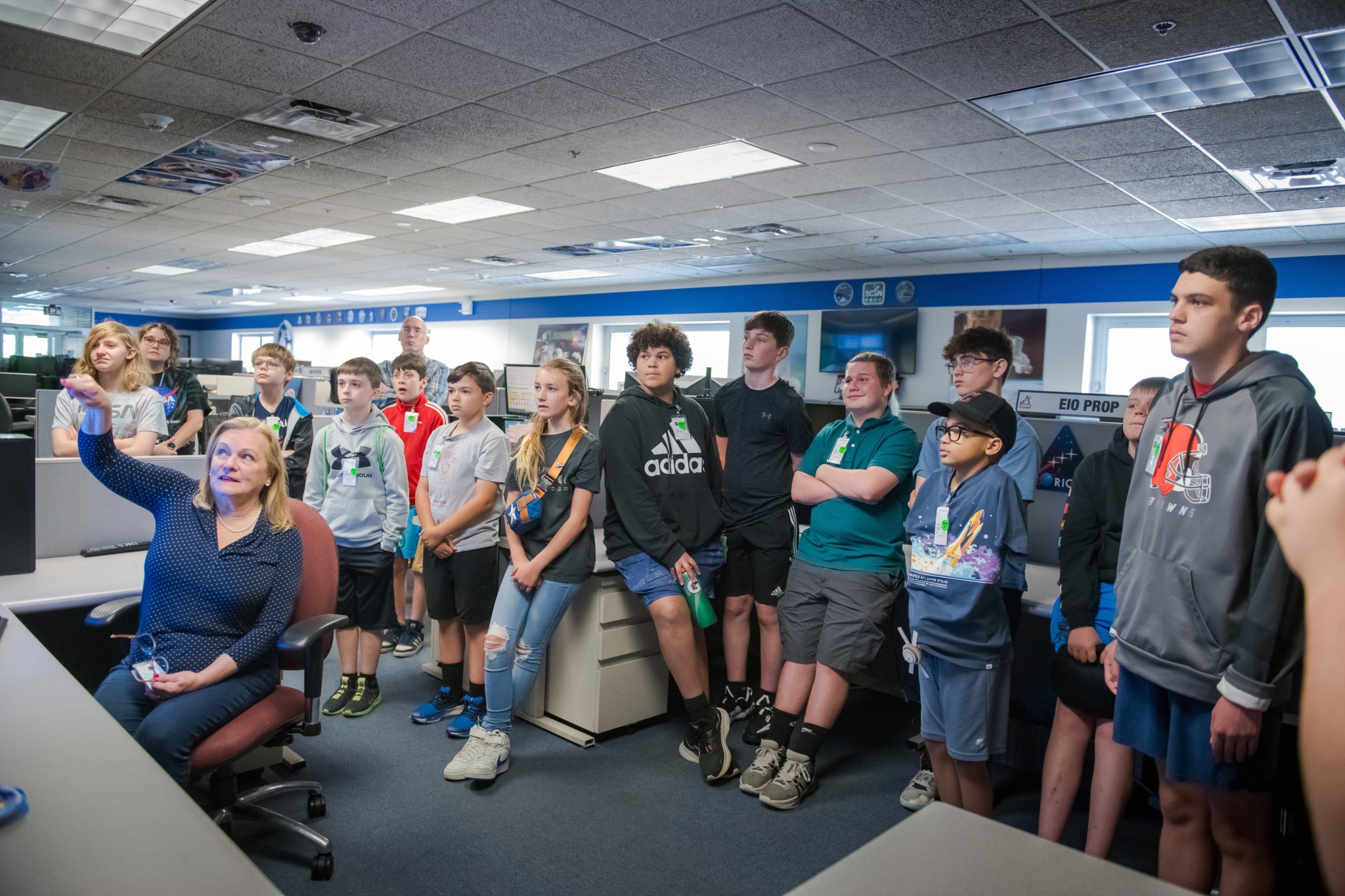 Woman, seated left, points at monitors while a group of students listen.
