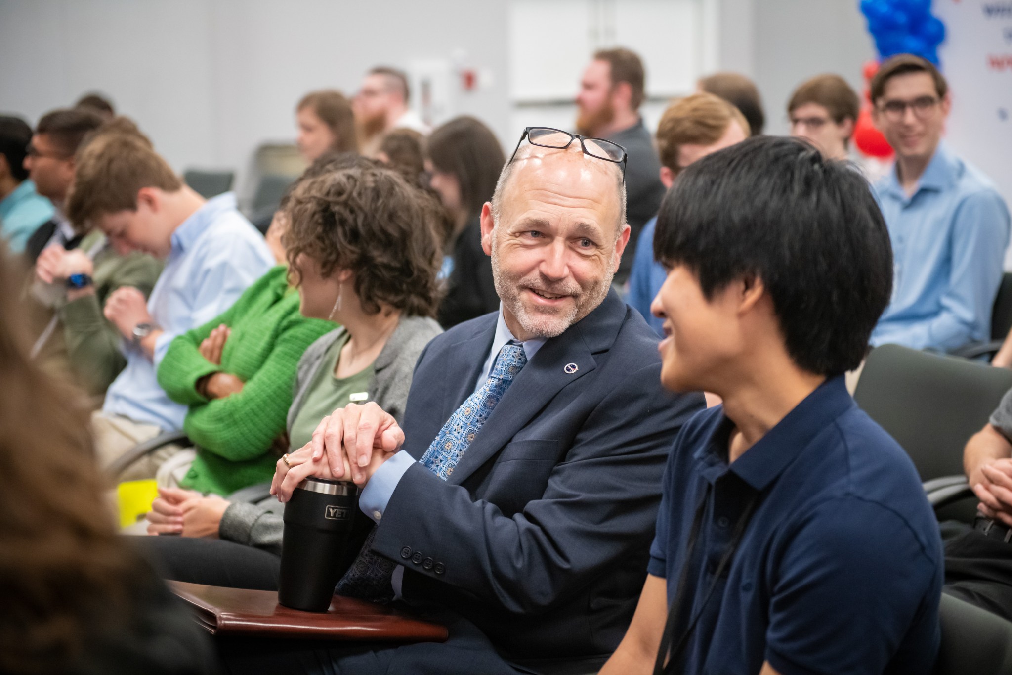 Center Director Dr. Jimmy Kenyon talks with a student among the many seated in the audience.