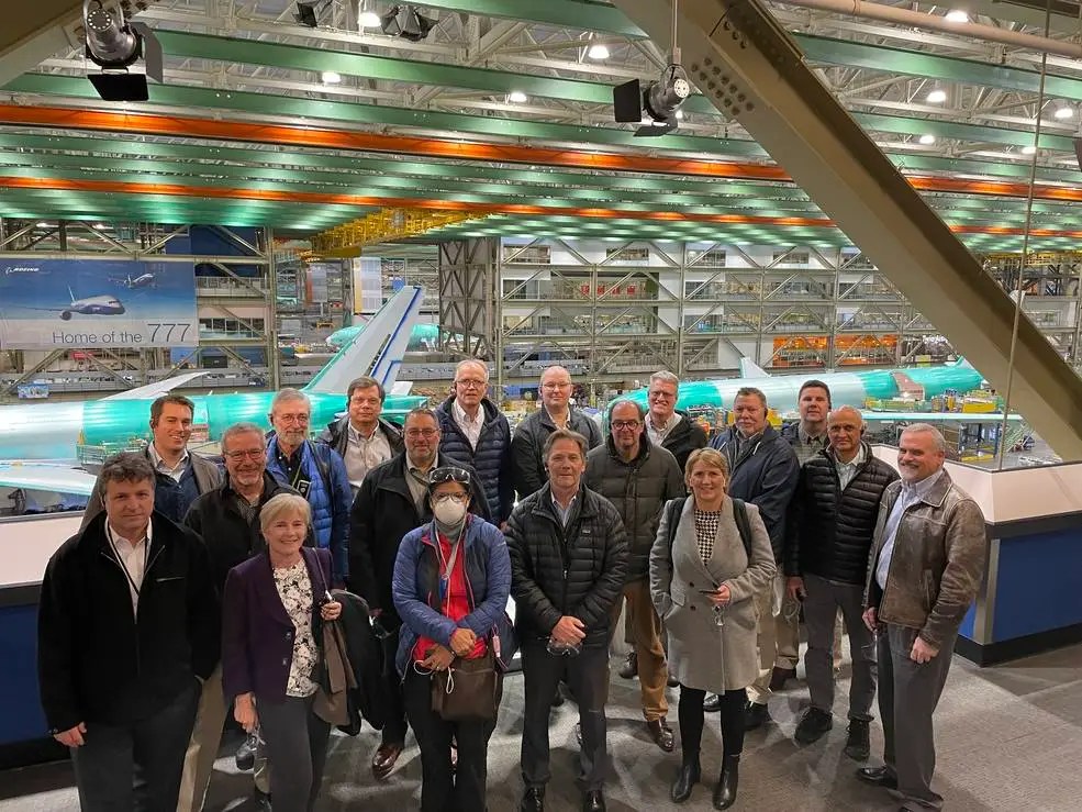 A group of people pose in fronts of two large Boeing airliners under construction behind them.