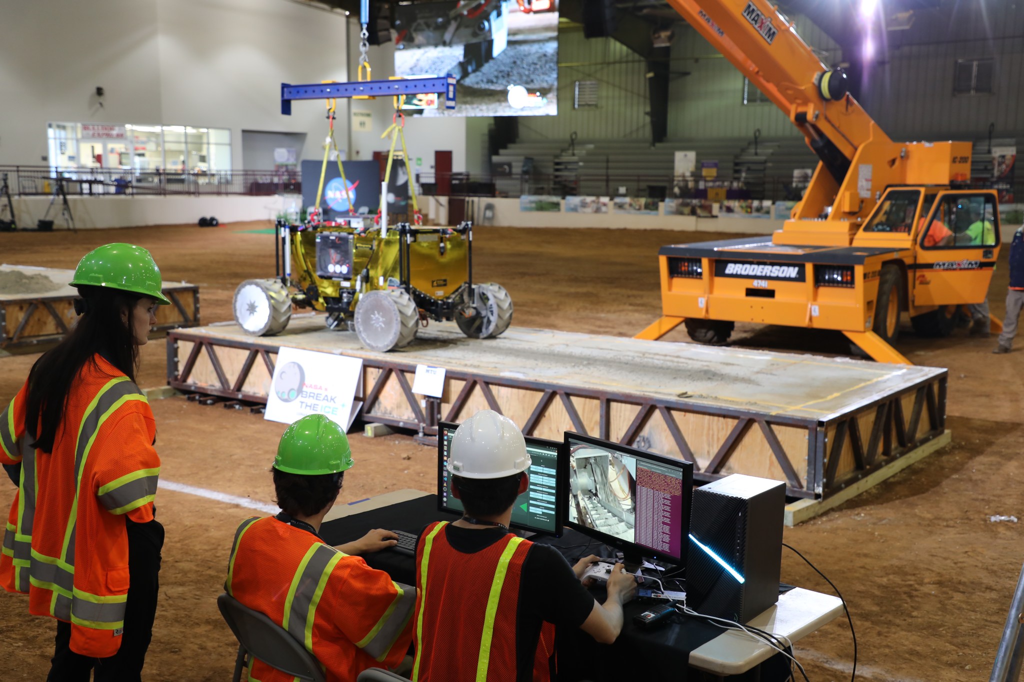 “HuskyWorks,” a team from Michigan Technological University’s Planetary Surface Technology Development Lab, tests the excavation tools of a robot on a concrete slab, held by a gravity-offloading crane on June 12 at NASA’s Break the Ice Lunar Challenge at Alabama A&M’s Agribition Center in Huntsville, Alabama. Led by Professor Paul van Susante, the team aimed to mimic the conditions of the lunar South Pole, winning an invitation to use the thermal vacuum chambers at NASA’s Marshall Space Flight Center to continue robotic testing.