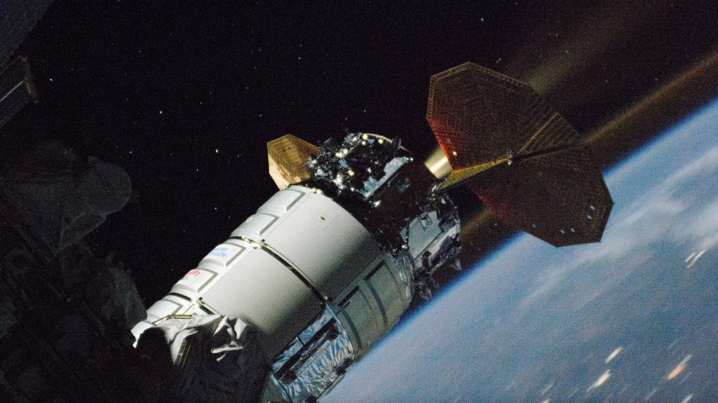 Northrop Grumman's Cygnus space freighter, attached to the Unity module, is pictured firing its single engine boosting the International Space Station's orbital altitude. This long-duration photograph also shows an atmospheric glow hovering above Earth's horizon.