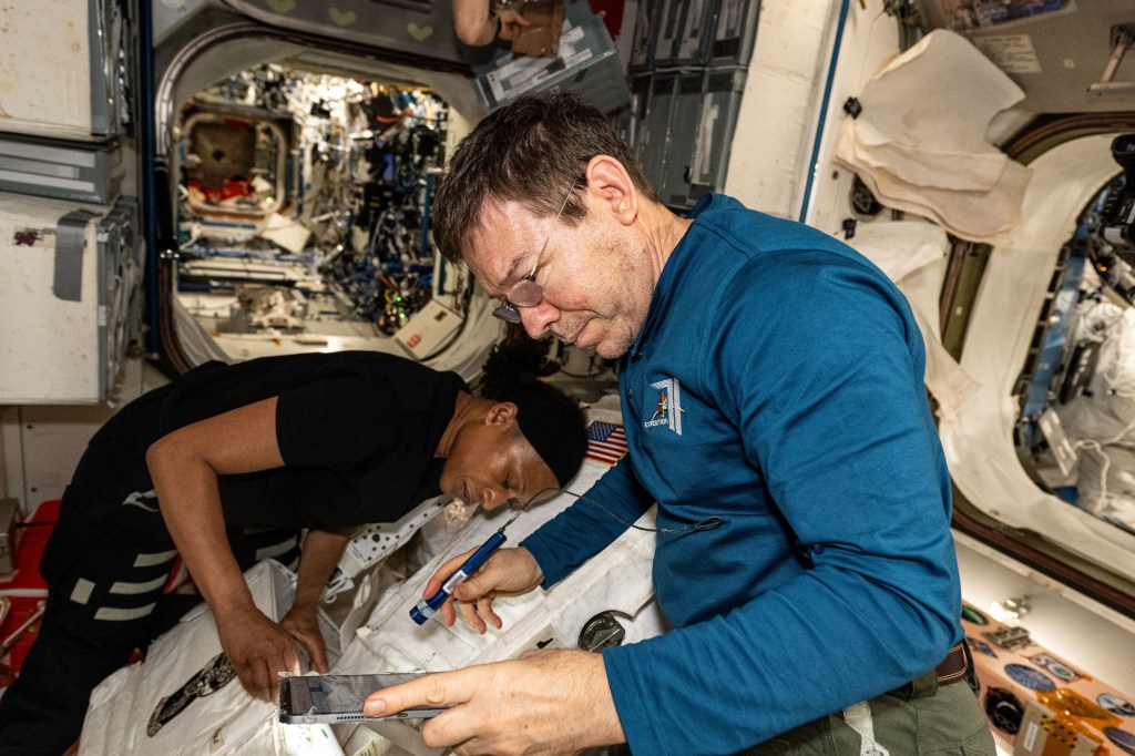 Expedition 71 Flight Engineers Jeanette Epps and Mike Barratt, both NASA astronauts, practice installing safety components on a spacesuit inside the International Space Station's Unity moduile.