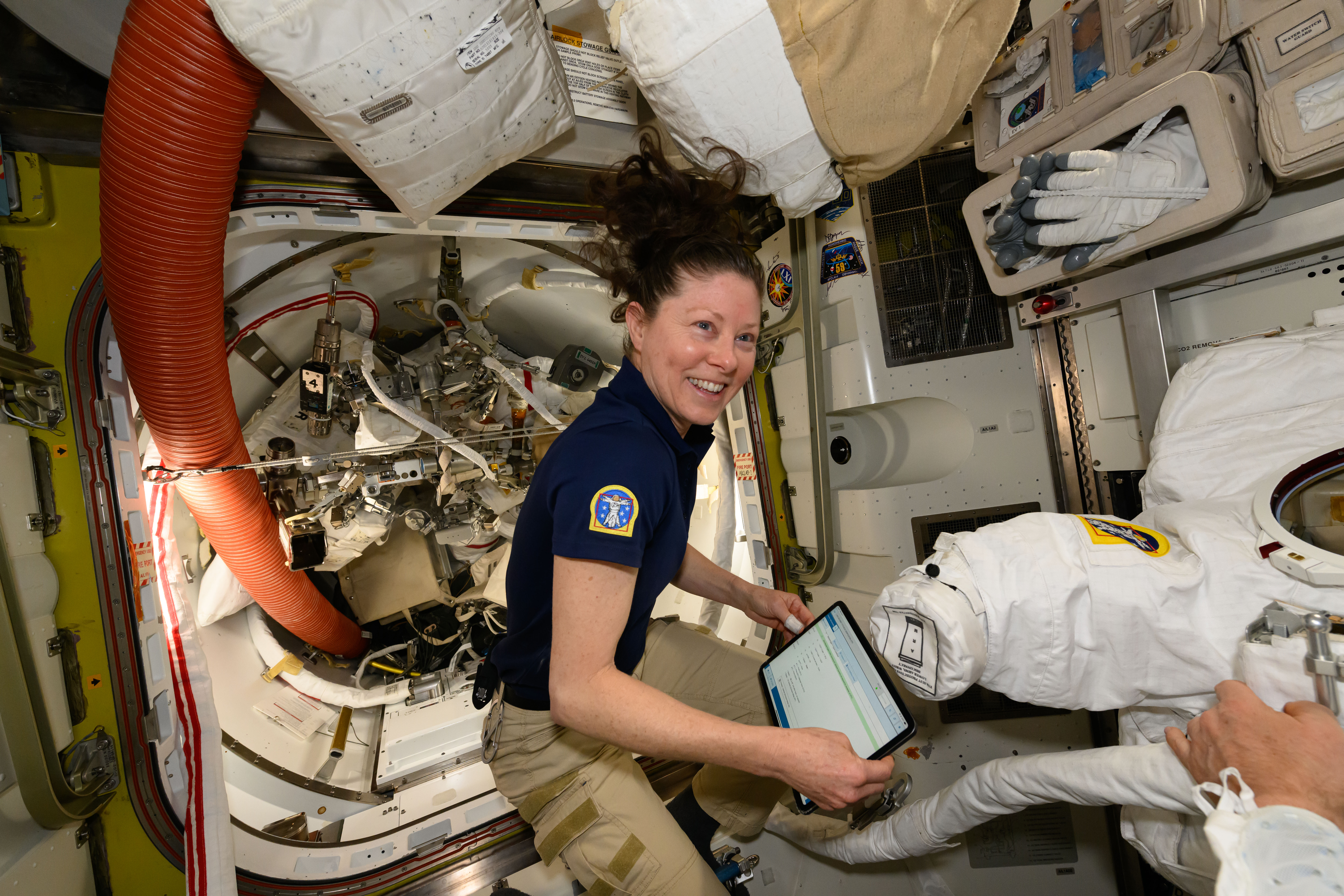 NASA astronaut and Expedition 71 Flight Engineer Tracy C. Dyson works inside the International Space Station's Quest airlock and checks procedures on a computer tablet to prepare a spacesuit for a fit verification.