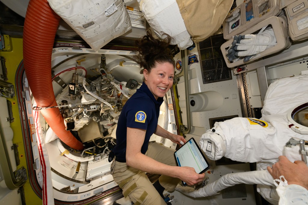 NASA astronaut and Expedition 71 Flight Engineer Tracy C. Dyson works inside the International Space Station's Quest airlock and checks procedures on a computer tablet to prepare a spacesuit for a fit verification.