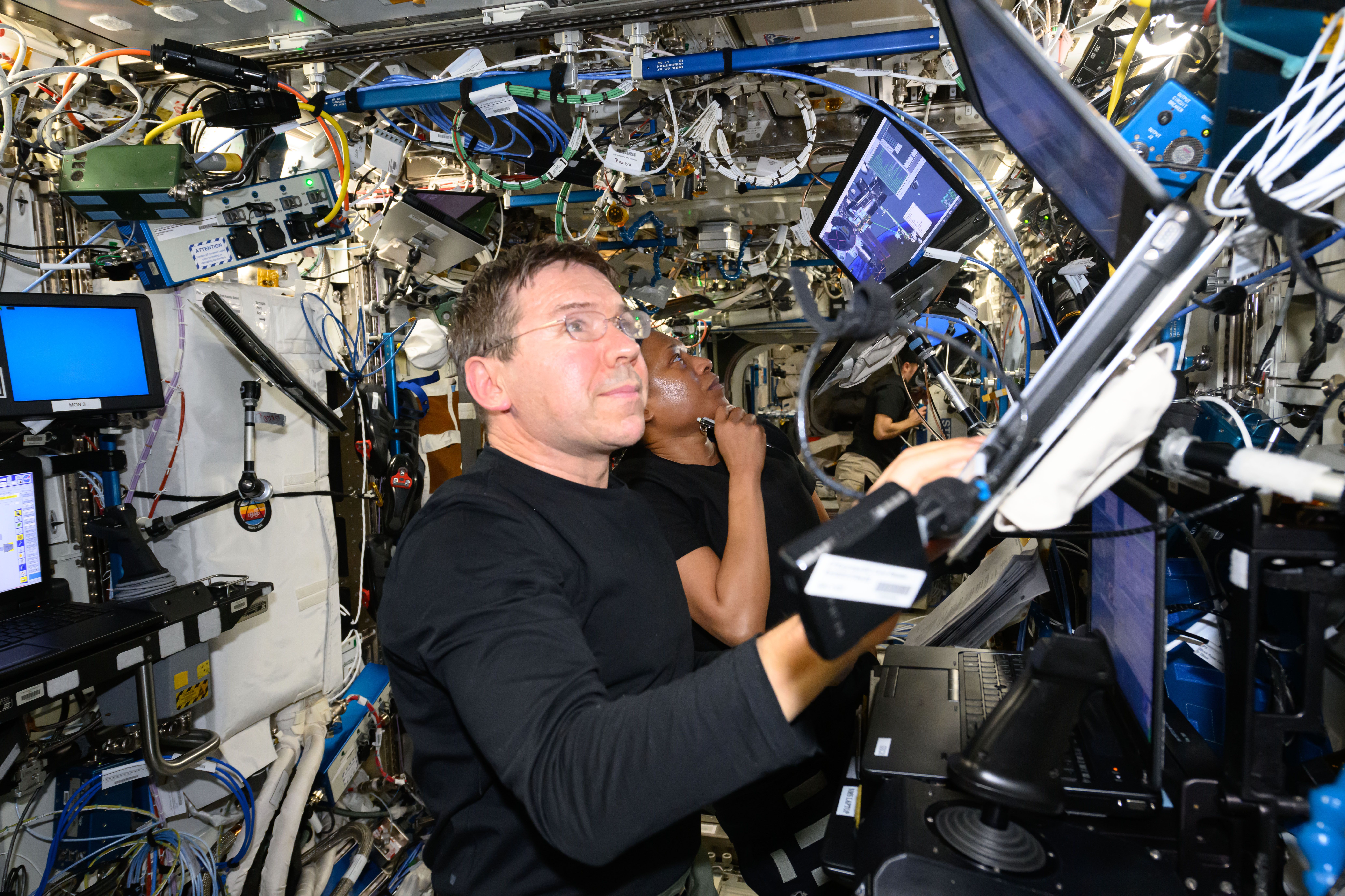 iss071e180163 (June 10, 2024) --- Expedition 71 Flight Engineers Mike Barratt and Jeanette Epps, both NASA astronauts, look at computer monitors on the Destiny laboratory module's robotics workstation that controls the Canadarm2 robotic arm.
