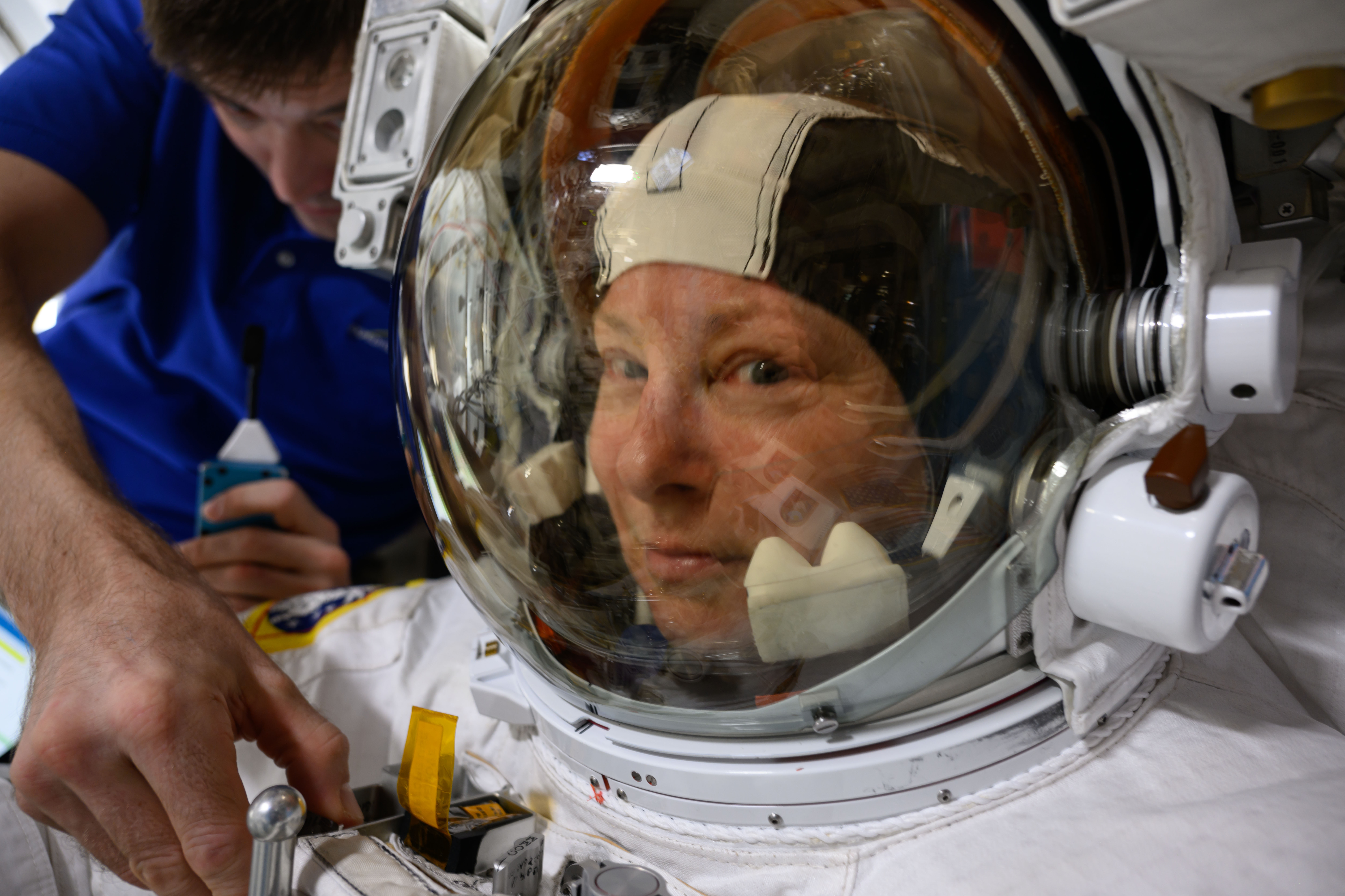 NASA astronaut and Expedition 71 Flight Engineer Tracy C. Dyson is pictured in her spacesuit prior to the start of a science and maintenance spacewalk that ended early on June 24, 2024, after her suit experienced a water leak in the service and cooling umbilical unit. Fellow astronaut and flight engineer Matthew Dominick is pictured assisting Dyson inside the International Space Station's airlock.