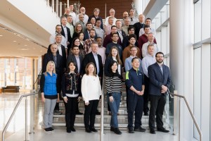 A group of 42 researchers stand on a staircase inside a building to pose for a group photo.