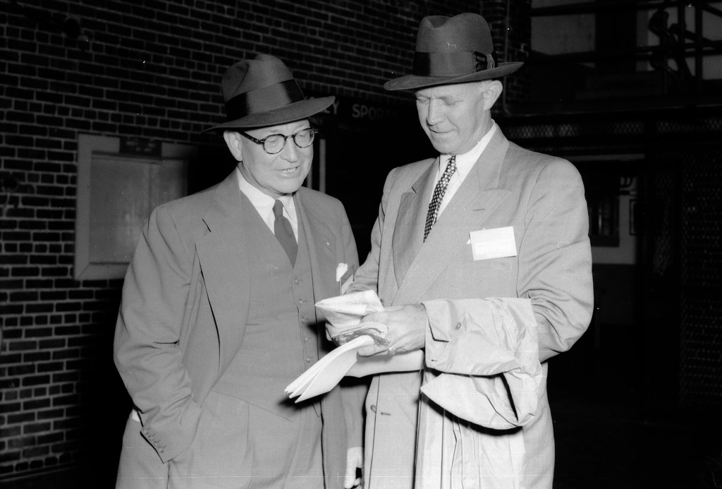 Two men look at paper.