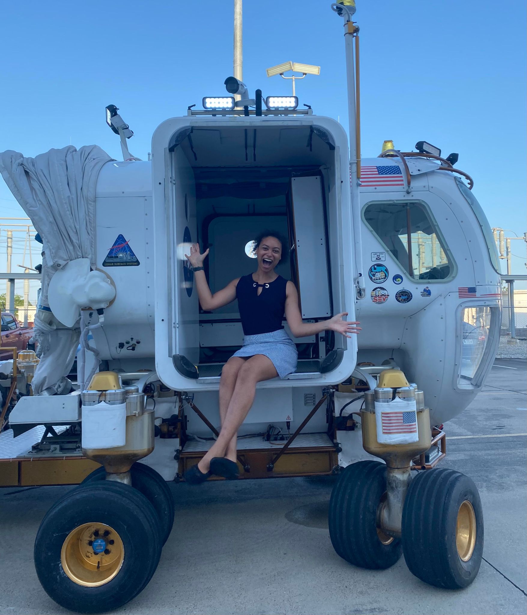 A young woman sits inside the airlock on the side of a lunar rover mockup.