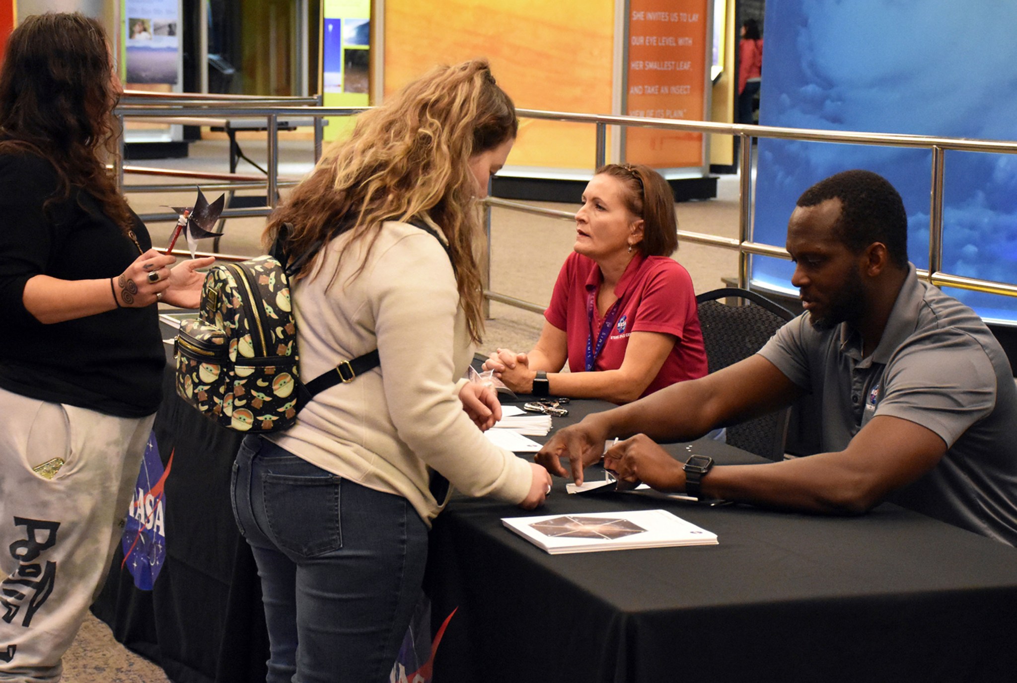 Two women standing and talking to two NASA employees sitting at an exhibit table.