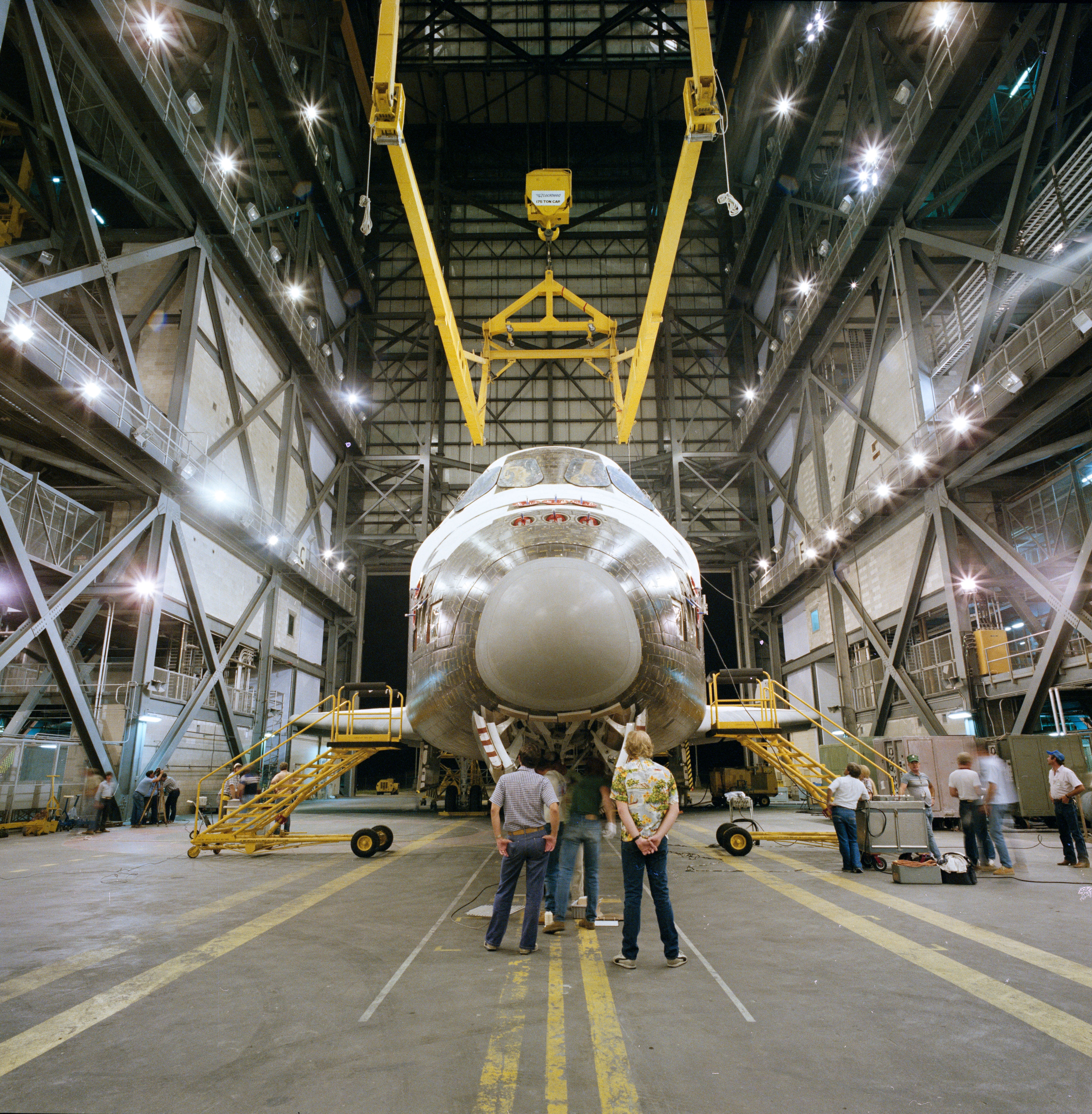 Workers in the Vehicle Assembly Building (VAB) at NASA’s Kennedy Space Center in Florida lift Discovery to mate it with its external tank and solid rocket boosters