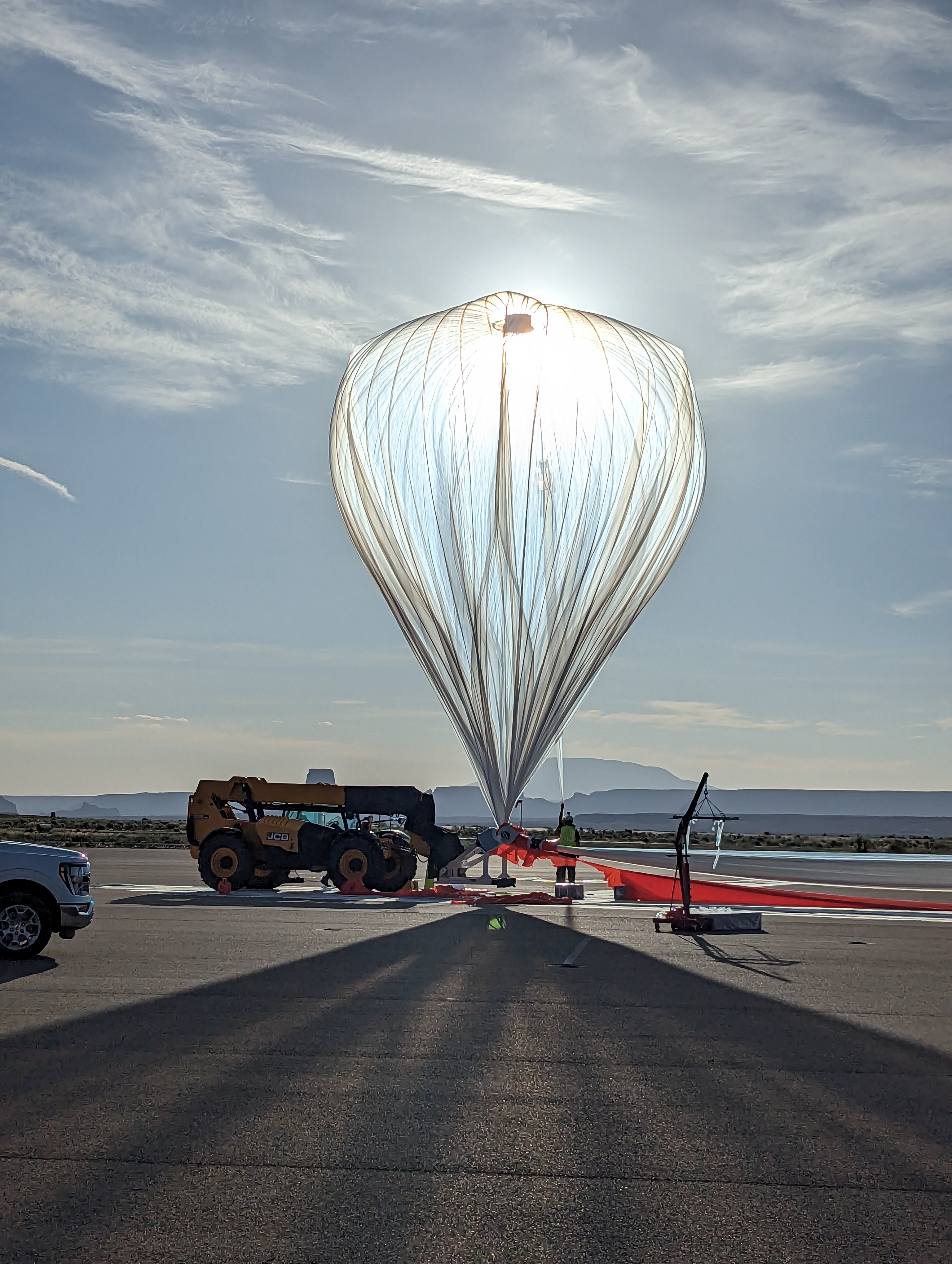 Inflated high-altitude balloon with the sun behind it sits on the tarmac