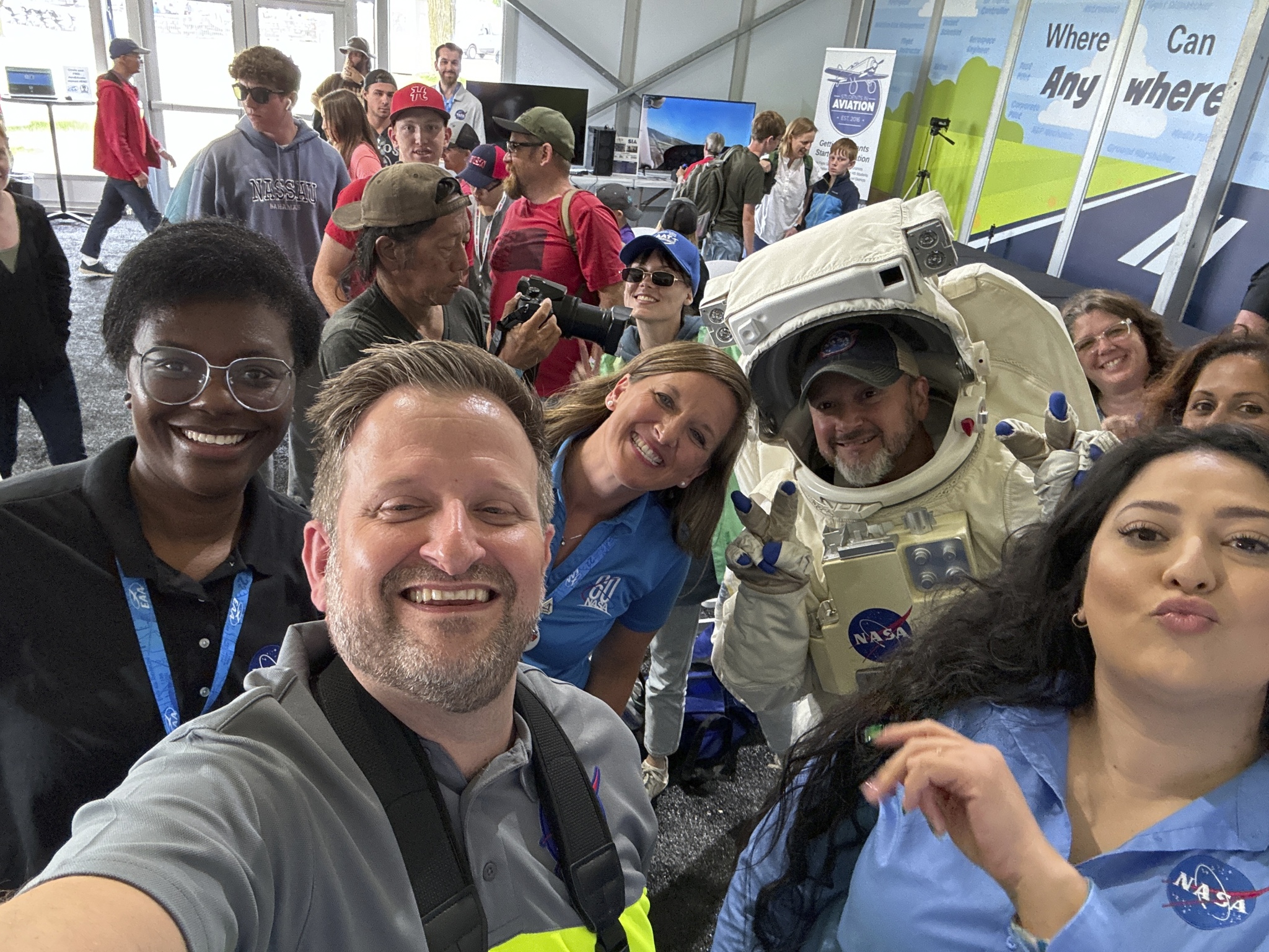 A group of adults pose for a selfie. One of the people is wearing an astronaut space suit.