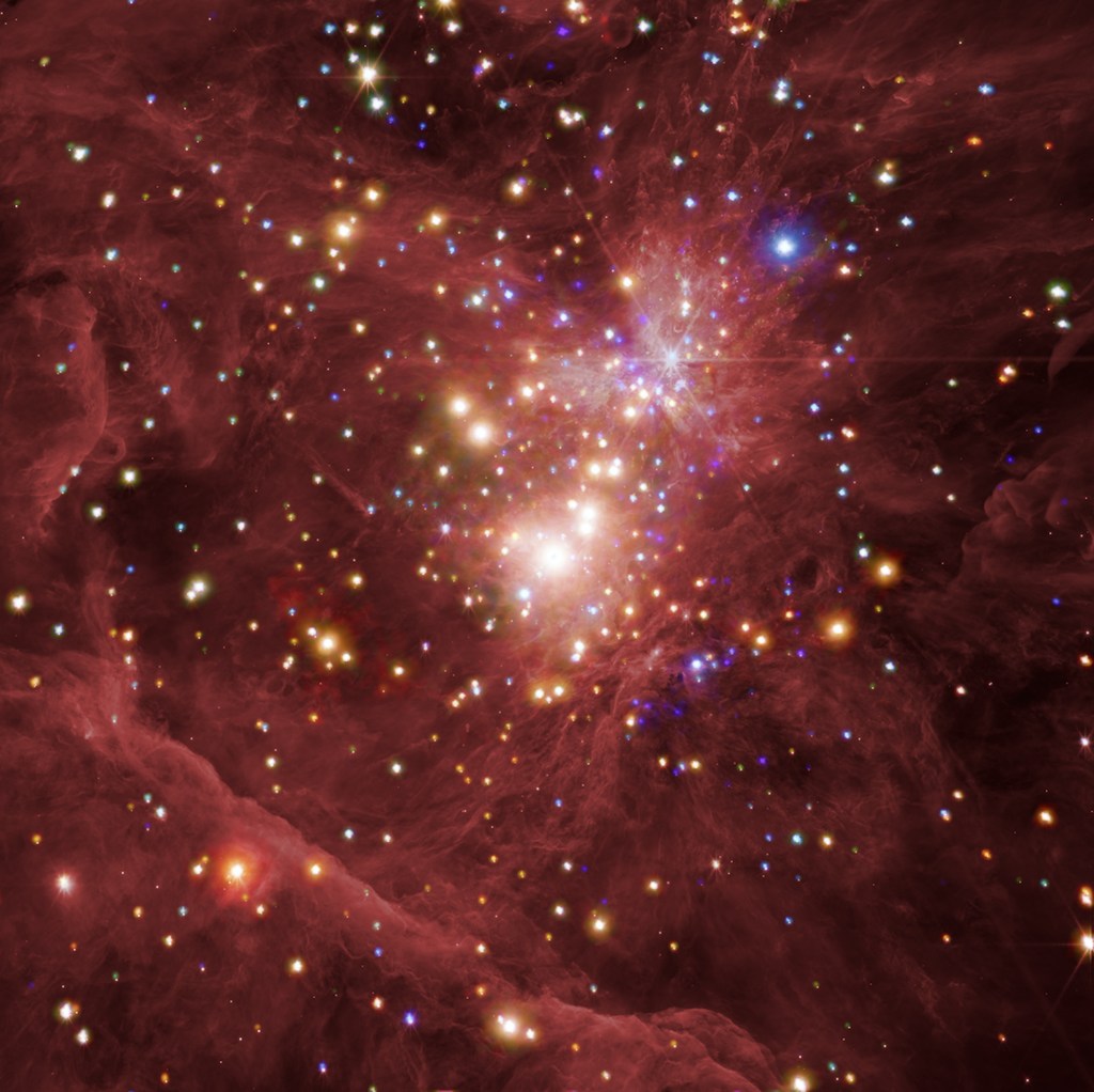 The young star nursery at the heart of the Orion Nebula resembles a dense, stringy, dusty rose cloud, peppered with thousands of glowing golden, white, and blue stars. Layers of cloud around the edges of the image, and a concentration of bright stars at its distant core, help convey the depth of the nebula.