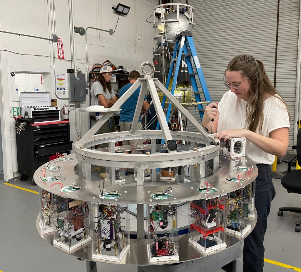 Woman holds a screwdriver while attaching payloads to a circular frame.