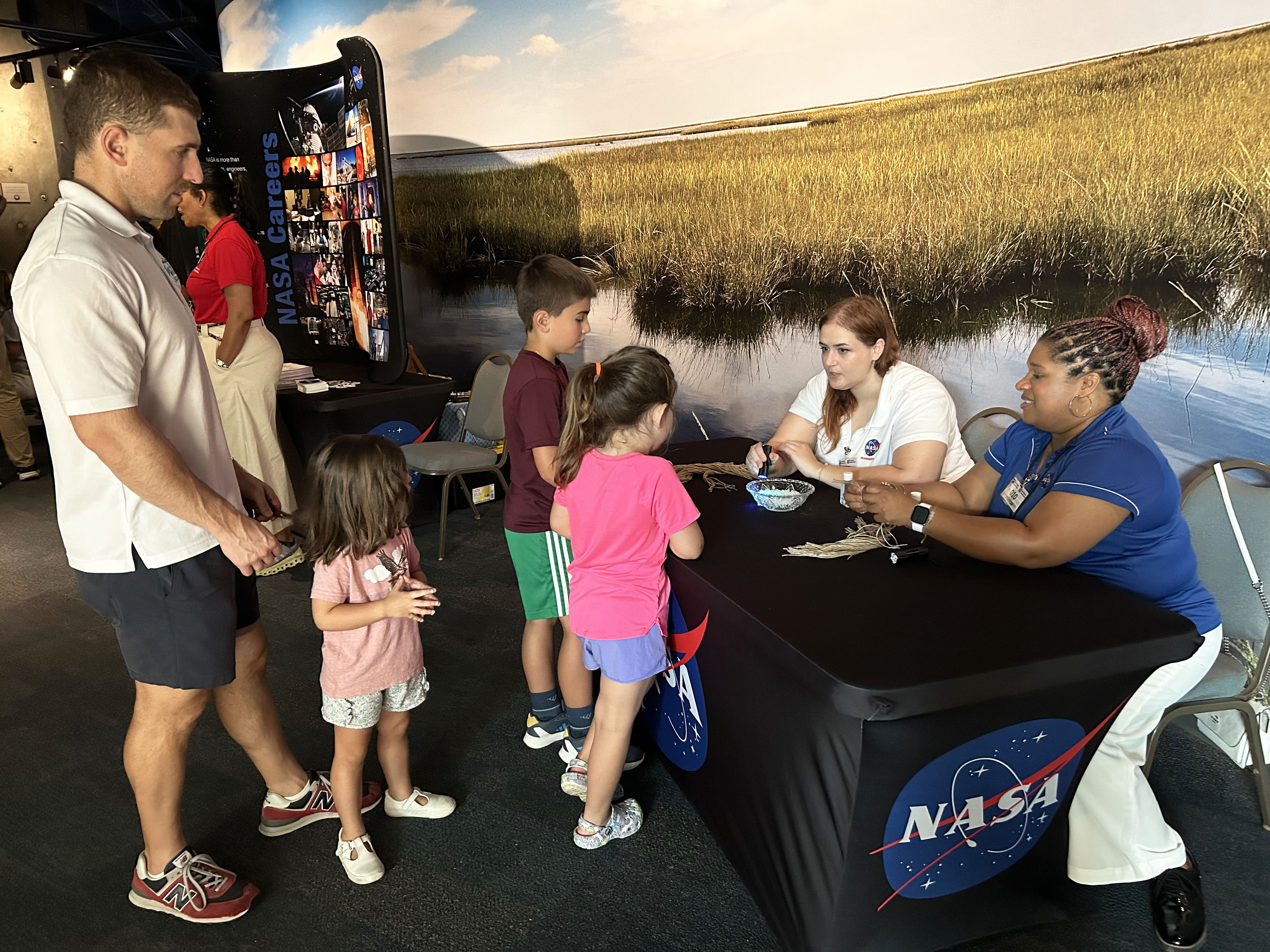A small group of children gather at the NASA interactive exhibit were two NASA representatives assist