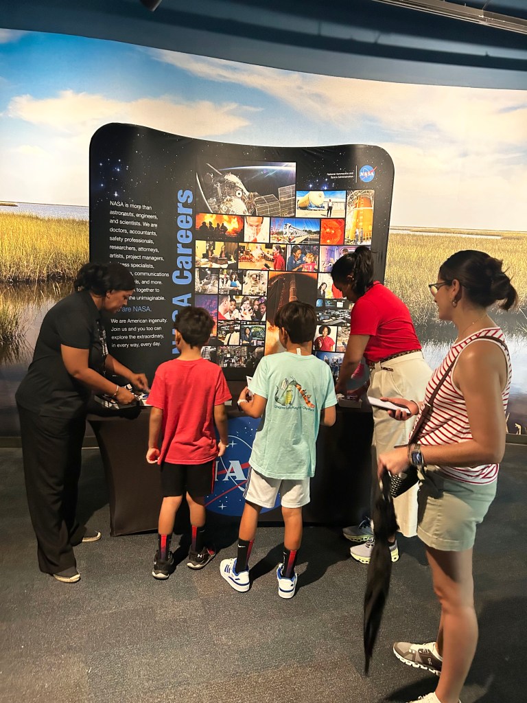 Two NASA representatives engage with young visitors who stopped at the NASA booth at Essesnce Fest