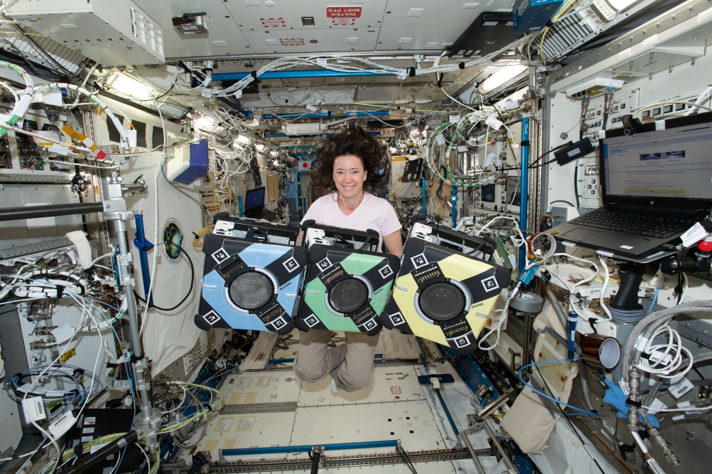 NASA astronaut Megan McArthur floats in the Japanese Experiment Module on ISS with three cube-shaped free flying robots.