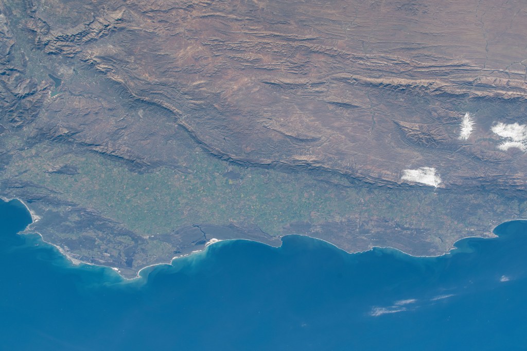 The steep slopes of the Great Escarpment descend toward to the coastal lowlands at the southernmost tip of South Africa in this photograph from the International Space Station as it orbited 269 miles above.