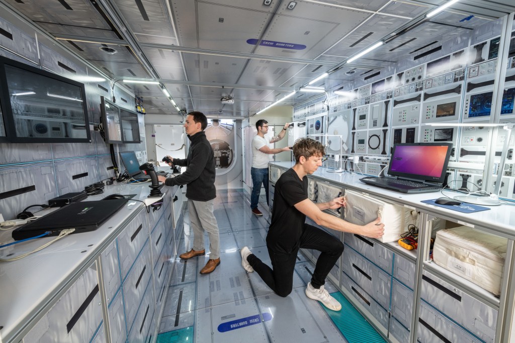 Three NASA engineers conduct habitability testing inside a mockup of a Gateway space station module.
