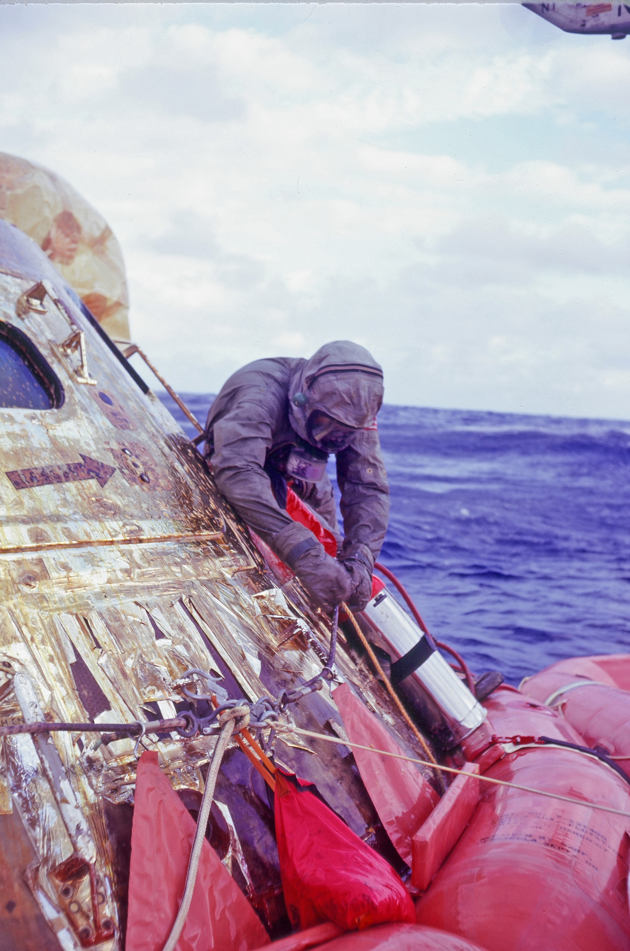 Wearing his Biological Isolation Garment (BIG), Clancy Hatleberg, the decontamination officer, sets up his decontamination canisters. He’s already handed the astronauts their BIGs, who are donning them inside the spacecraft