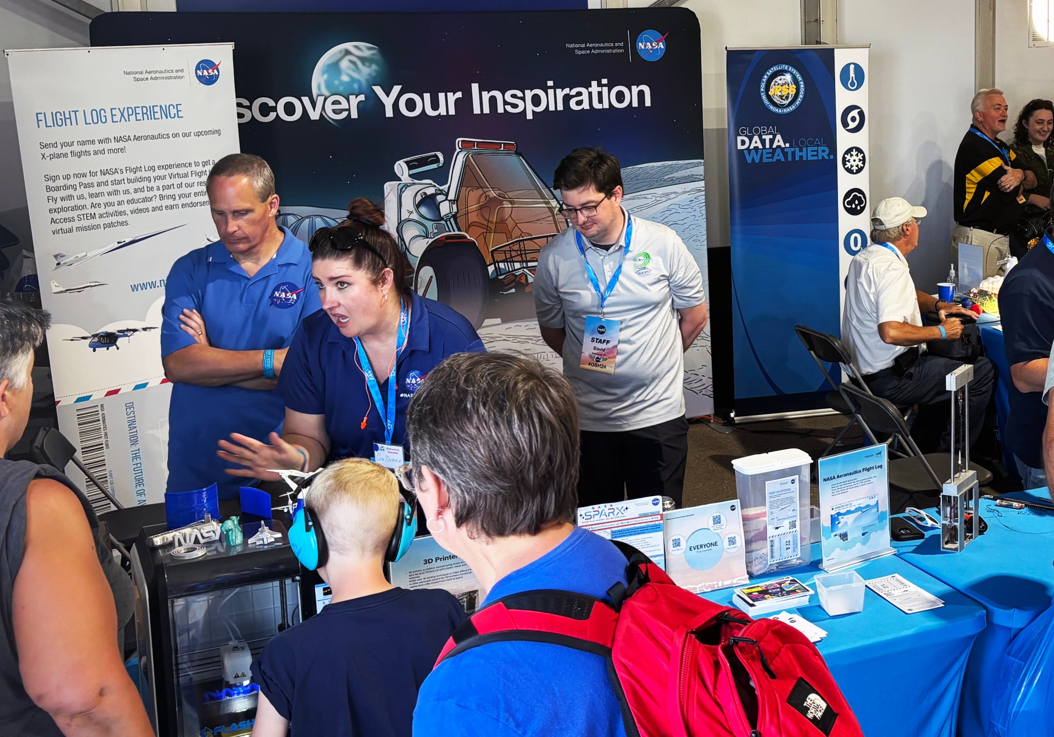 A group of people stand around an exhibit table filled with brochures and fact sheets.