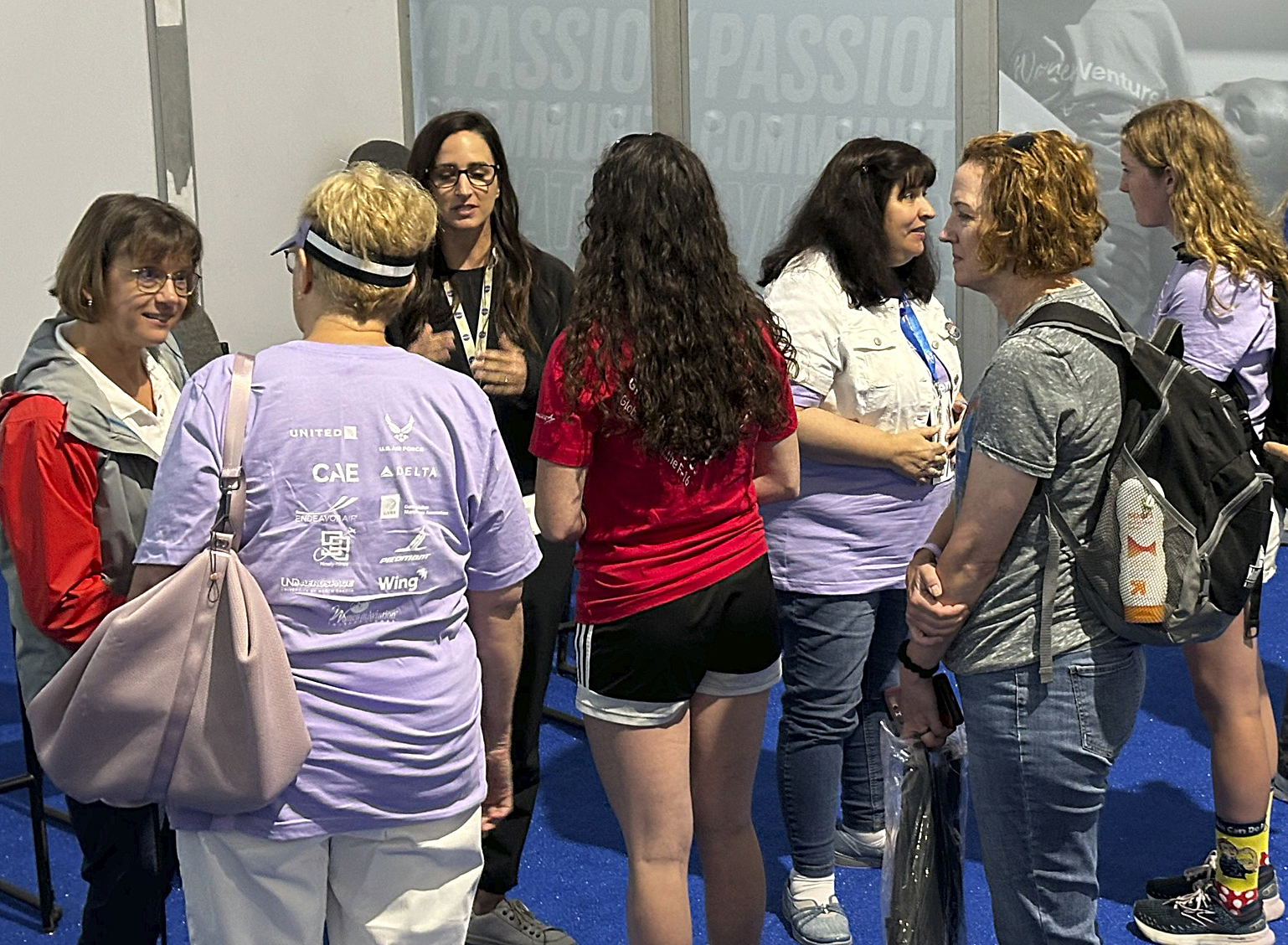 A group of women dressed in casual clothing talk with each other while standing.