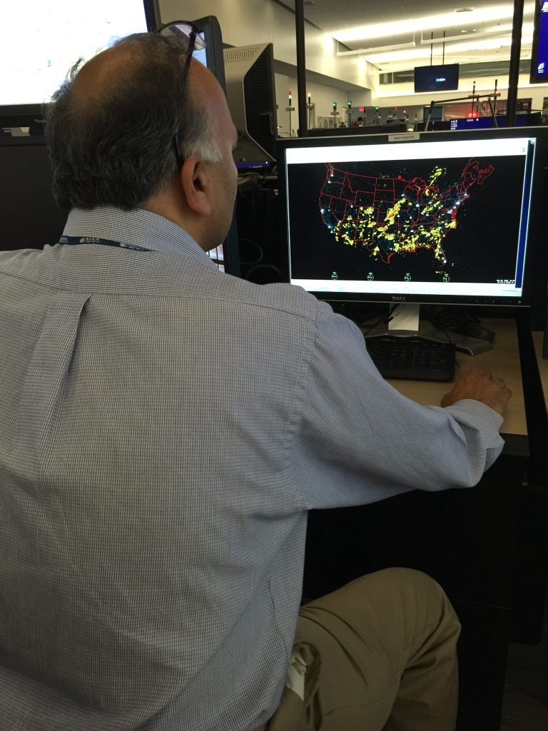 A man sits at a desk with a computer display showing convective weather across an outline of the United States.