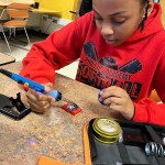 A young student holds a soldering iron.