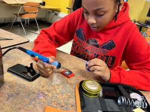 A young student holds a soldering iron.