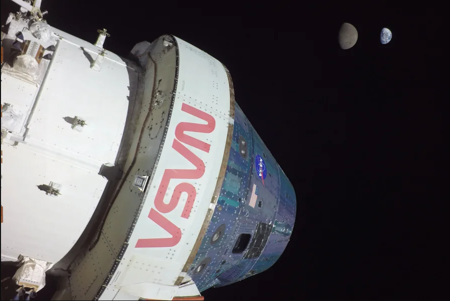 Photograph of the Orion capsule in space with the Earth and its moon in the background