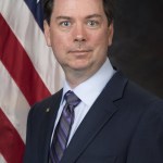 This is an official photograph of Bryan Barmore, Senior Technical Advisor and Lead Systems Engineer of the Aeronautics Research Directorate at NASA’s Langley Research Center. Barmore is wearing a dark suit, a light blue button down shirt, and a grey tie with blue stripes. An American flag can be seen behind Barmore.